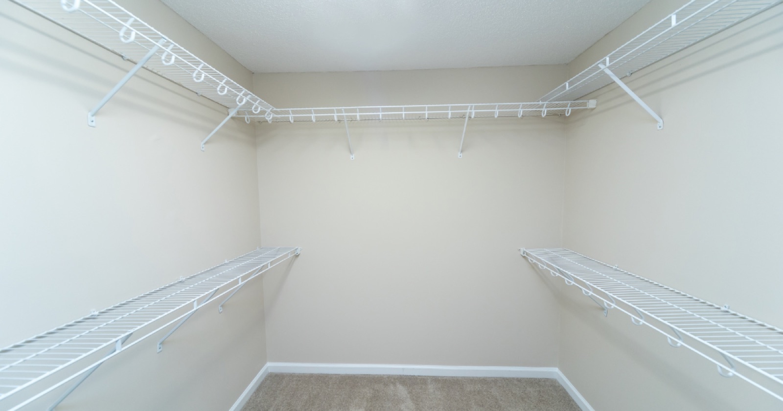 Empty walk-in closet with sagging builder-grade wire shelving and a single hanging rod on each wall